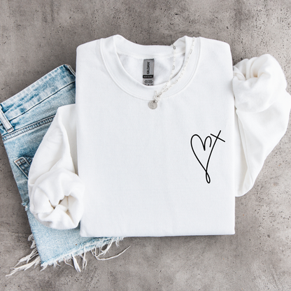 White youth sweatshirt flat lay with a small heart cross graphic on the front chest, styled with denim.