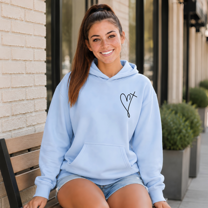 Woman wearing a light blue Jesus Has My Back hoodie with a small heart cross graphic on the front chest while seated outside.