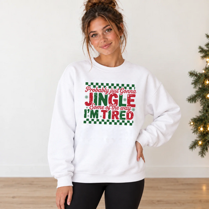 Woman in a white sweatshirt with red and green Jingle Some of the Way I'm Tired Christmas graphic beside a lit evergreen garland.
