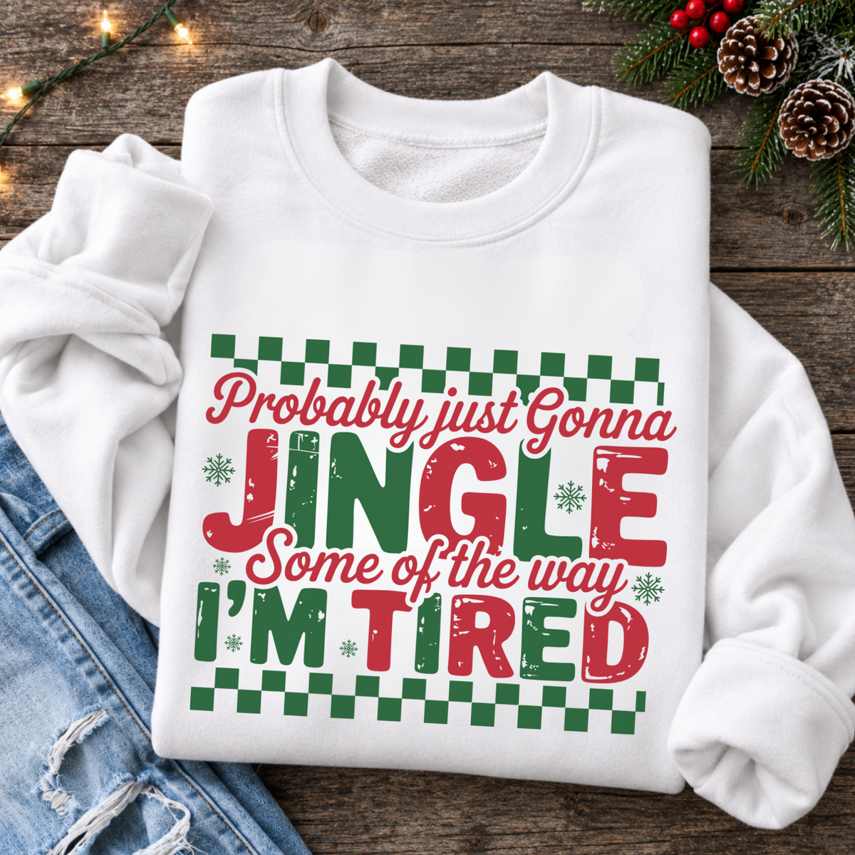 White sweatshirt flat lay with red and green Probably Just Gonna Jingle Some of the Way I'm Tired Christmas design, jeans and evergreen décor