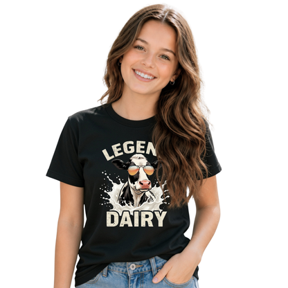 A smiling young girl wears a black T-shirt with a “LEGEND DAIRY” graphic showing a black-and-white cow in sunglasses splashing through milk, against a white background.