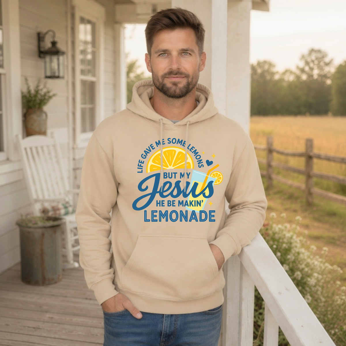 Man modeling a sand hoodie with the Life Gave Me Some Lemons, But My Jesus He Be Makin’ Lemonade faith graphic on a country porch.