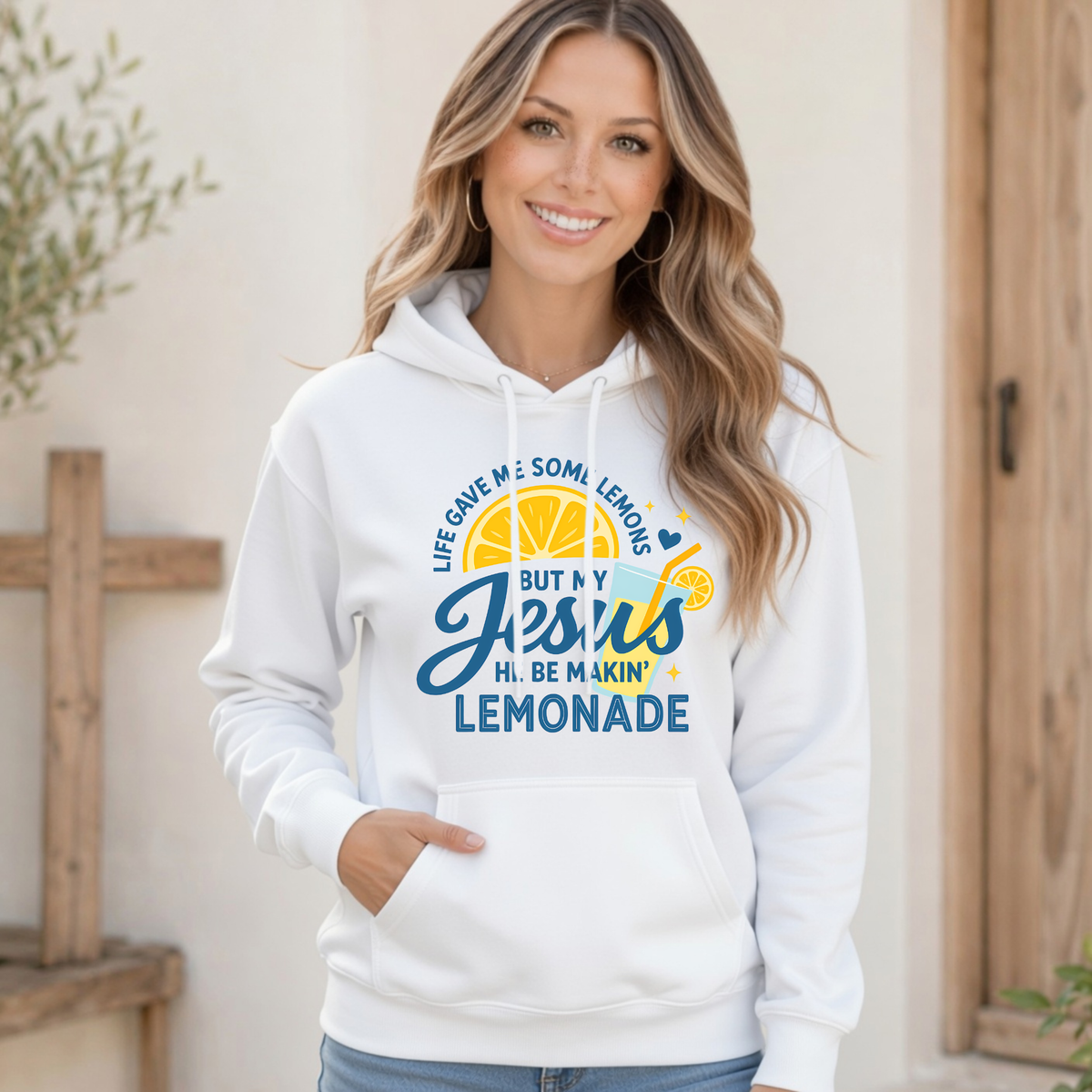 Smiling woman wearing a white hoodie printed with the Jesus Be Makin’ Lemonade lemon and lemonade cup graphic in blue and yellow.