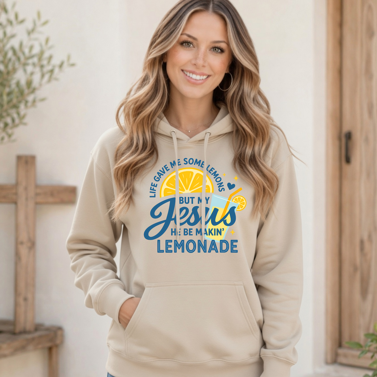 Woman modeling a sand hoodie with the Life Gave Me Some Lemons, But My Jesus He Be Makin’ Lemonade faith design on the front.
