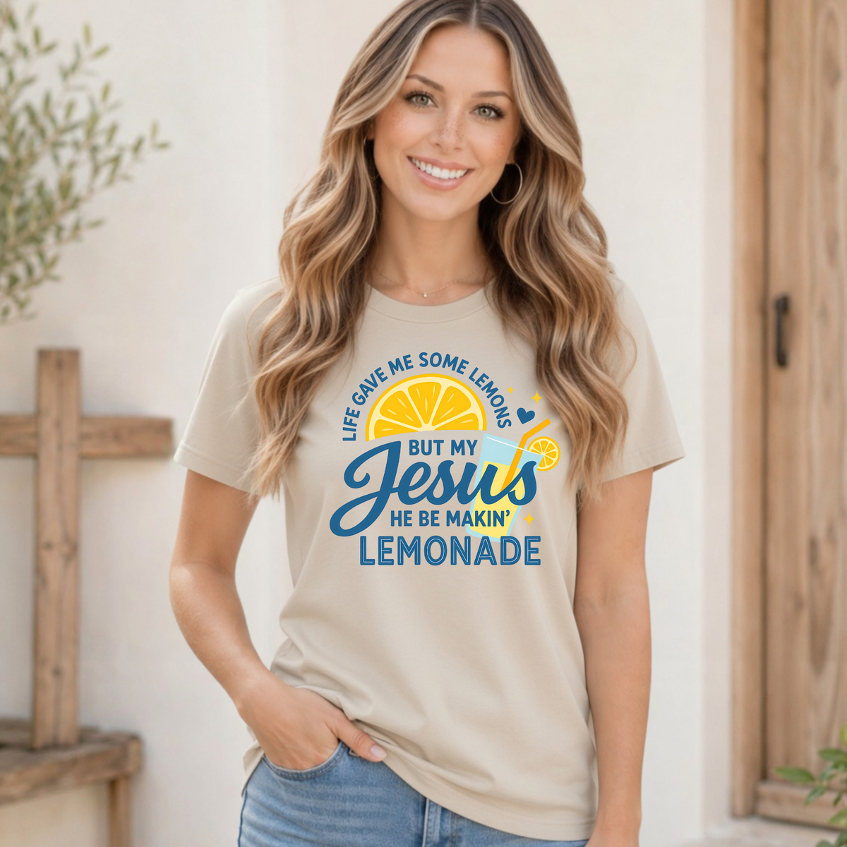 Woman in a sand T-shirt with the Life Gave Me Some Lemons, But My Jesus He Be Makin’ Lemonade faith graphic in blue and yellow.