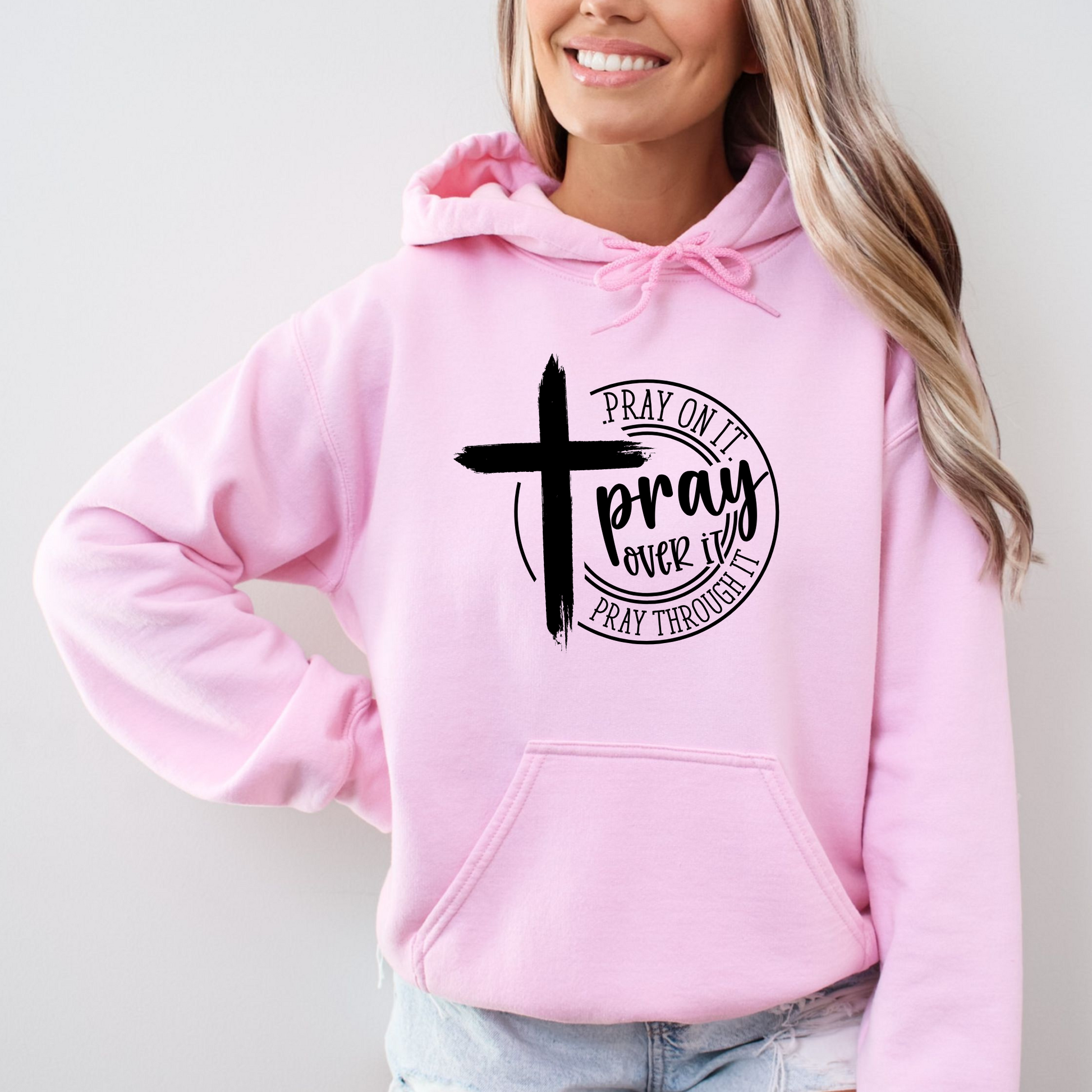 Woman wearing a bright light pink hoodie with a motivational message and cross symbol.