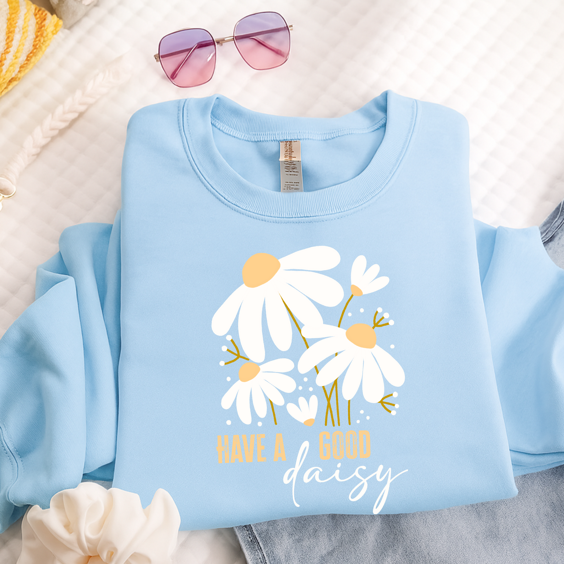Light blue sweatshirt with daisy design and text on a neutral background