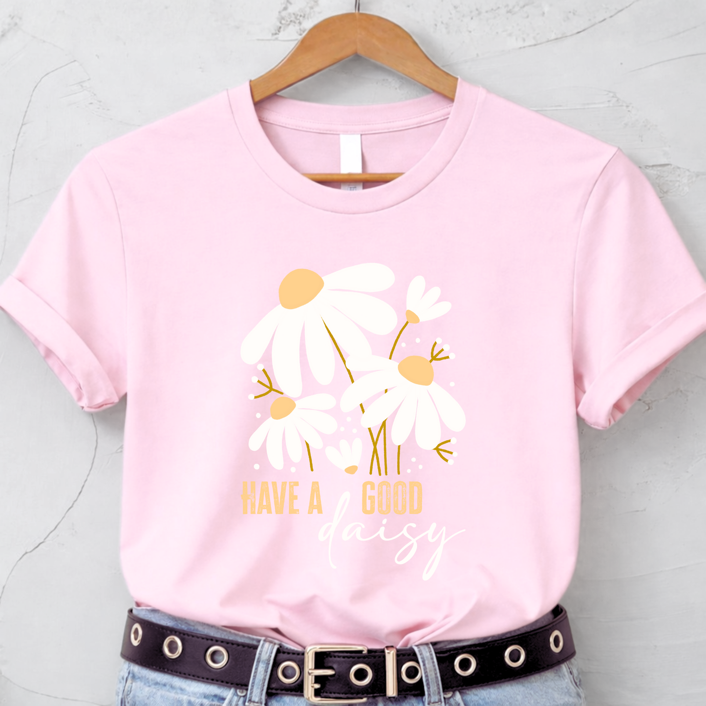 Pink t-shirt with floral design and text on a hanger against a light gray background