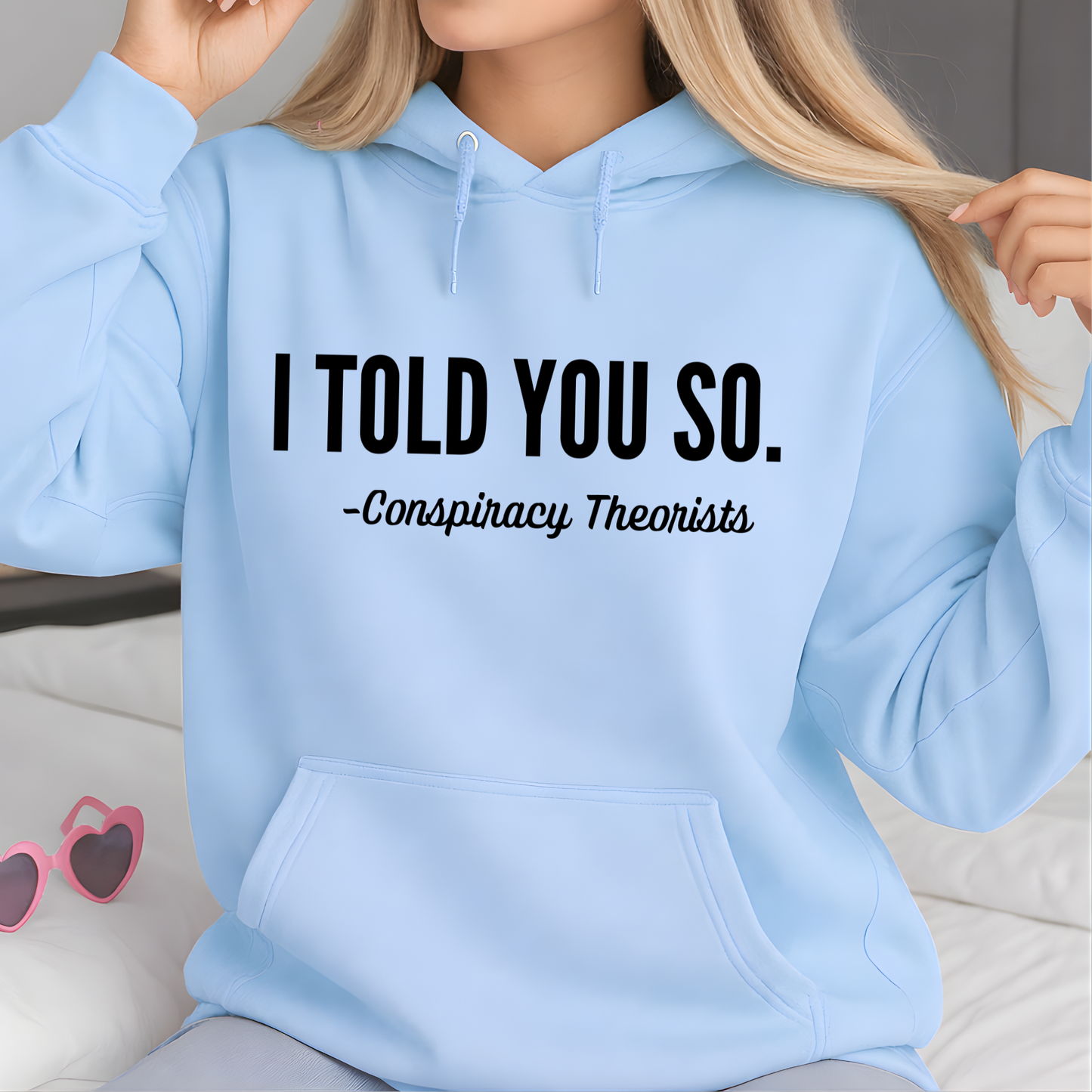Light blue hoodie with text 'I Told You So. - Conspiracy Theorists' worn by a woman.