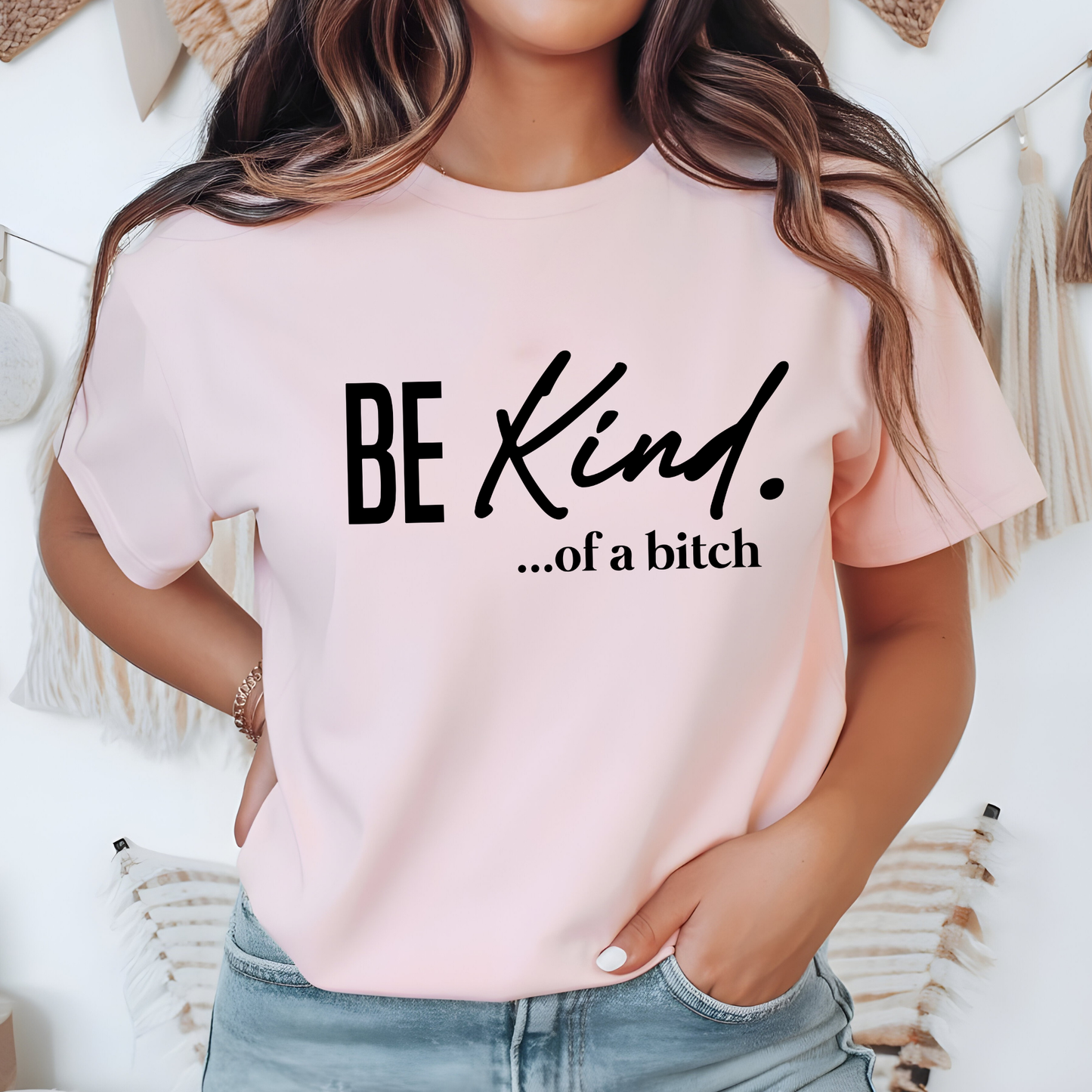 Light pink t-shirt with black “Be Kind…of a bitch” text styled in a cozy indoor setting
