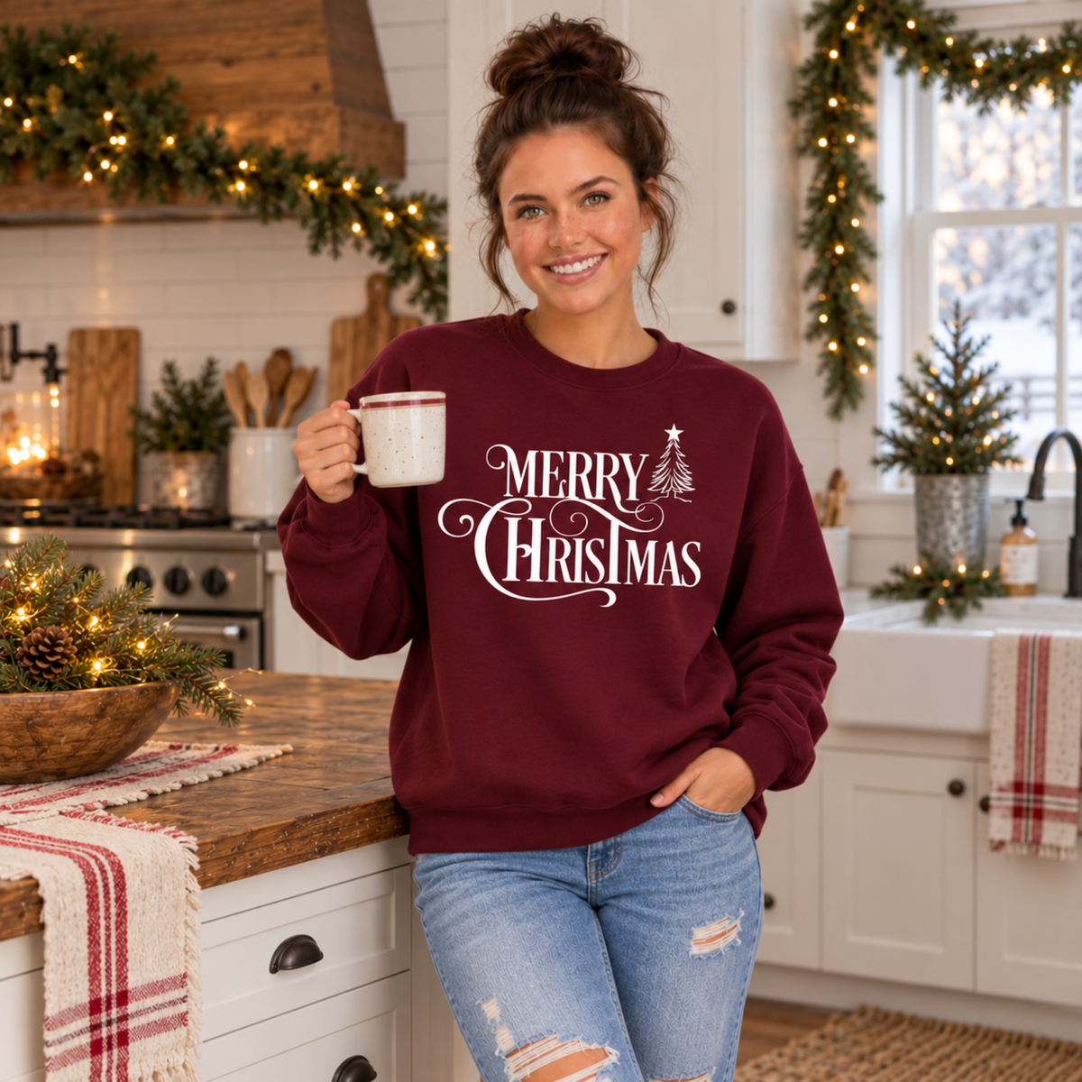 Model holding a mug in a holiday kitchen while wearing a maroon Merry Christmas crewneck sweatshirt.