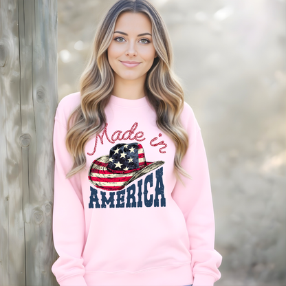 Woman wearing a pink sweatshirt with 'Made in America' design, standing against a wooden fence.