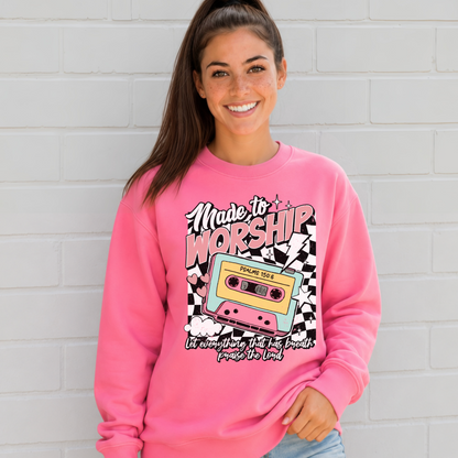 Woman wearing a Bright Pink Made to Worship crewneck sweatshirt with a retro cassette graphic against a white brick wall.