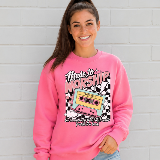 Woman wearing a Bright Pink Made to Worship crewneck sweatshirt with a retro cassette graphic against a white brick wall.