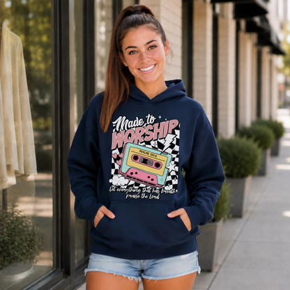 Woman wearing a navy Made to Worship hoodie with a retro cassette graphic outside a storefront.