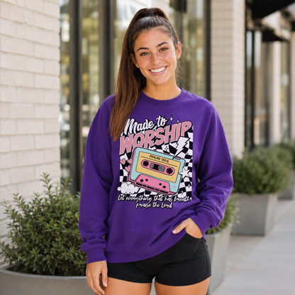 Woman wearing a purple Made to Worship crewneck sweatshirt with a retro cassette graphic outside a storefront.