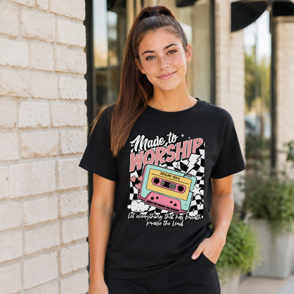 Woman wearing a black Made to Worship T-shirt with a retro cassette graphic outside a storefront.