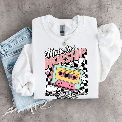 White Made to Worship youth crewneck sweatshirt flat lay with a colorful retro cassette graphic on a gray concrete background.