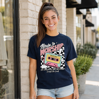 Woman wearing a navy Made to Worship T-shirt with a retro cassette graphic outside a storefront.