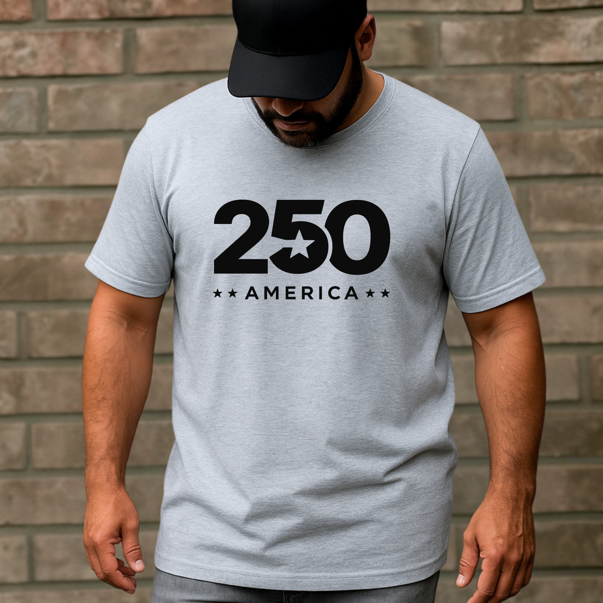 Man wearing a gray t-shirt with '250 America' print against a brick wall.