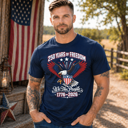 Man wearing a navy blue America 250 t-shirt with an eagle and text design, standing outdoors with an American flag in the background.