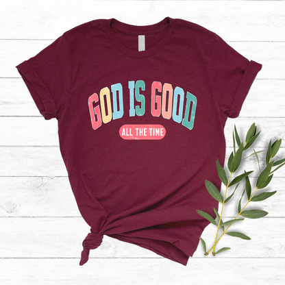 Flat lay of a Maroon T-shirt with 'God Is Good All the Time' in colorful text, perfect for Easter and Christian apparel.