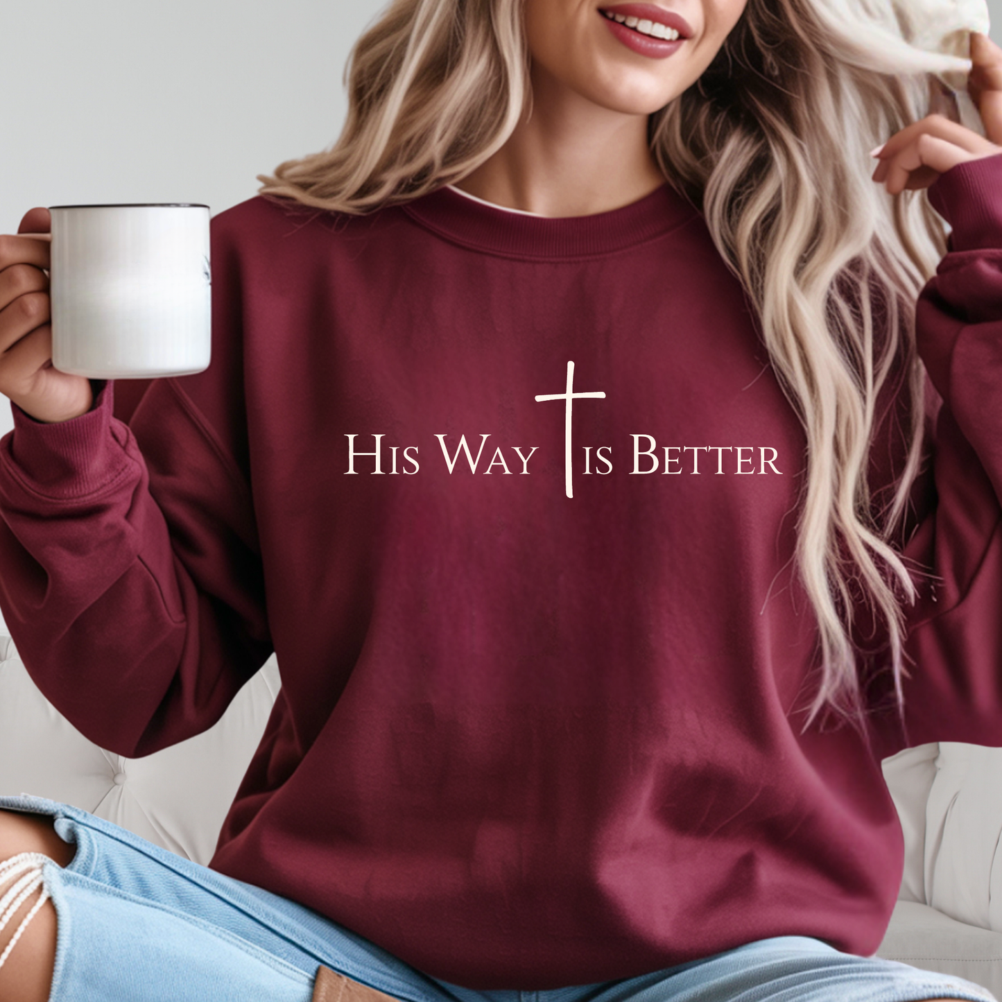 Woman wearing maroon “His Way Is Better” cross sweatshirt holding mug