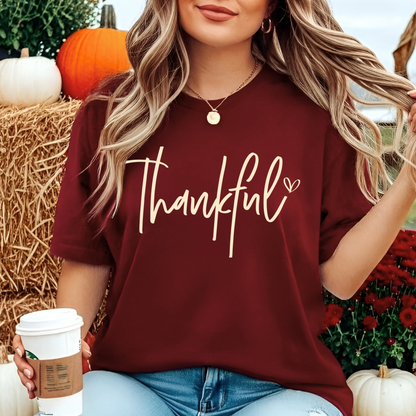 Woman holding coffee wearing maroon “Thankful” shirt, fall background