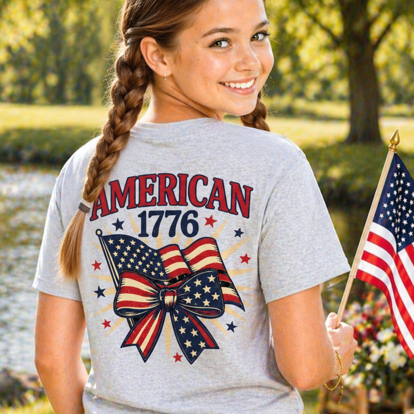 Girl wearing a t-shirt with 'American 1776' design, holding an American flag outdoors.
