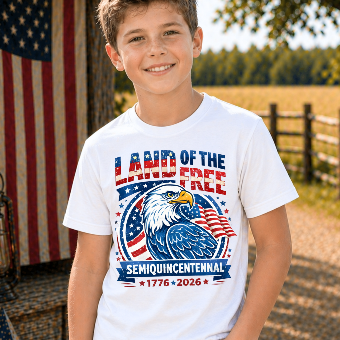 Child wearing a America 250 'Land of the Free' t-shirt with an eagle design, standing outdoors with an American flag in the background.
