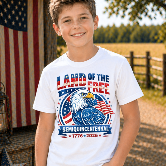 Child wearing a America 250 'Land of the Free' t-shirt with an eagle design, standing outdoors with an American flag in the background.