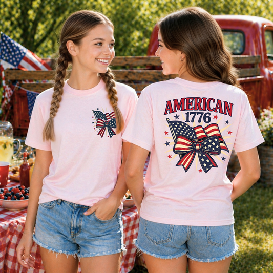Two girls wearing pink t-shirts with American flag designs, standing outdoors with a red truck and American flags in the background.