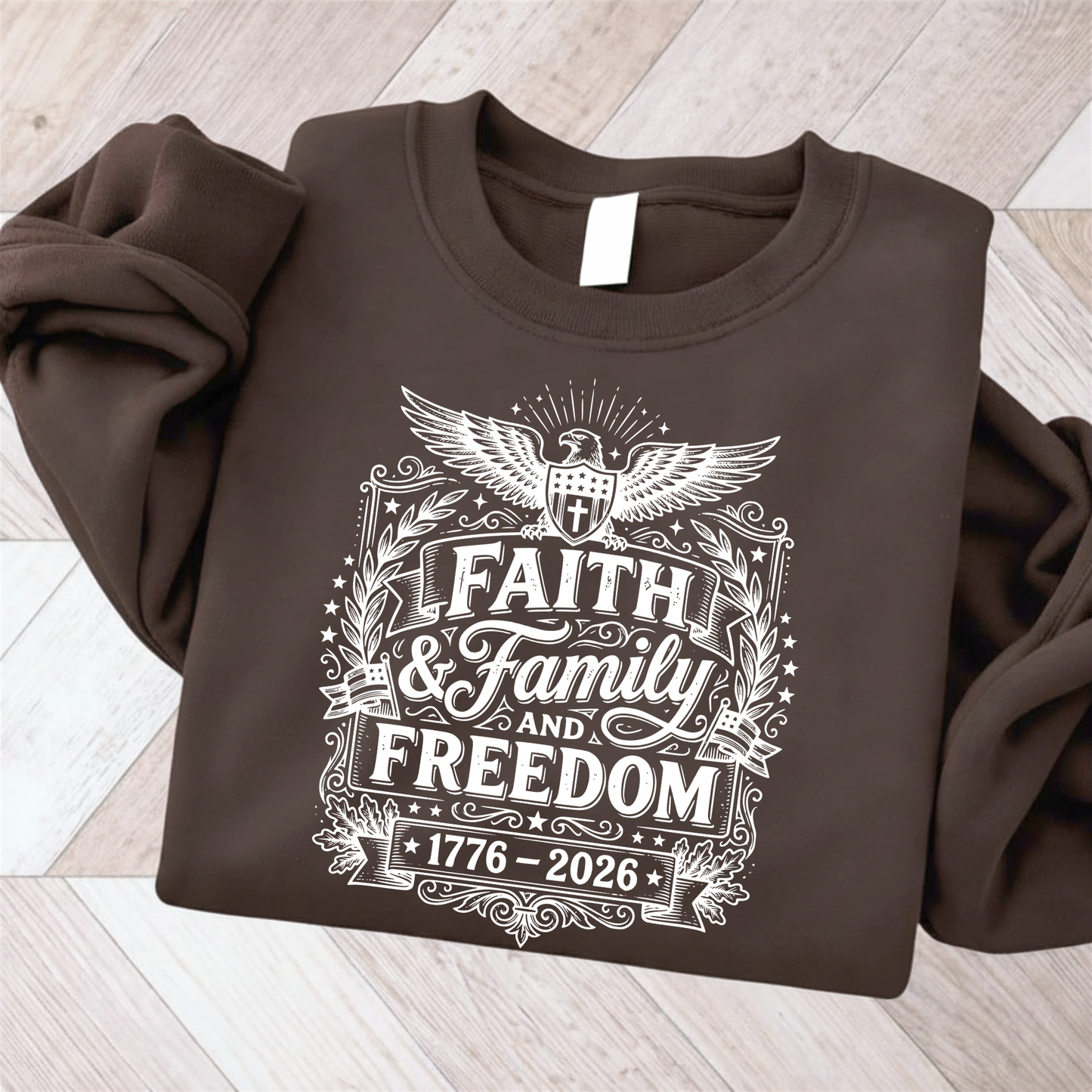 Brown sweatshirt with 'Faith & Family and Freedom 1776-2026' text on a wooden surface