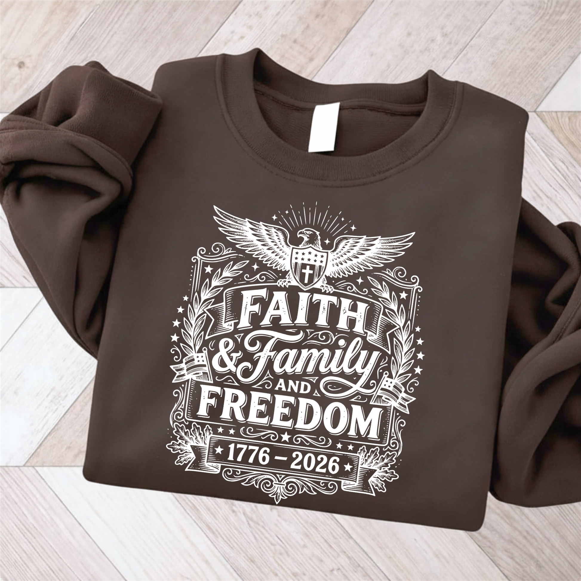 Brown sweatshirt with 'Faith & Family and Freedom 1776-2026' text on a wooden surface