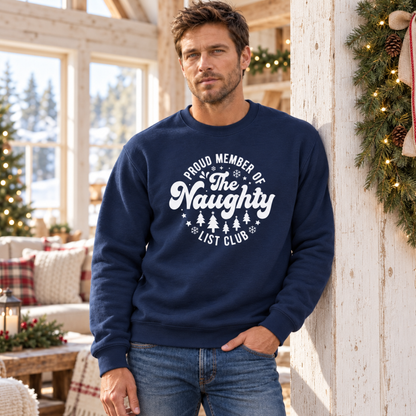 Man wearing a navy crewneck sweatshirt with a white Proud Member of the Naughty List Club design in a festive living room.