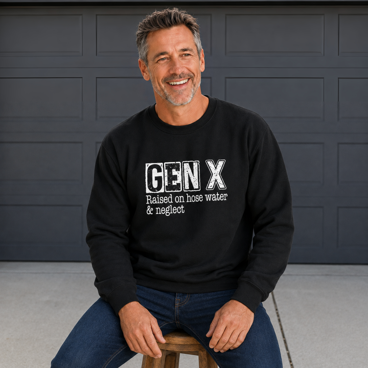 Man wearing a black Gen X crewneck sweatshirt with distressed “Raised on hose water & neglect” lettering in front of a dark garage door.