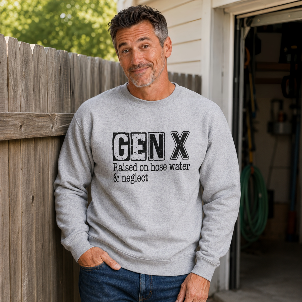 Man wearing a sports gray Gen X crewneck sweatshirt with distressed “Raised on hose water & neglect” lettering by a garden hose.