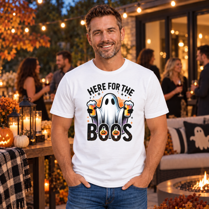 Man wearing a white T-shirt featuring a ghost holding two beers with Here For The Boos text at an outdoor Halloween party.