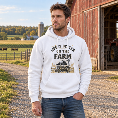 Man in a white Life Is Better on the Farm hoodie outside a red barn and fenced pasture.