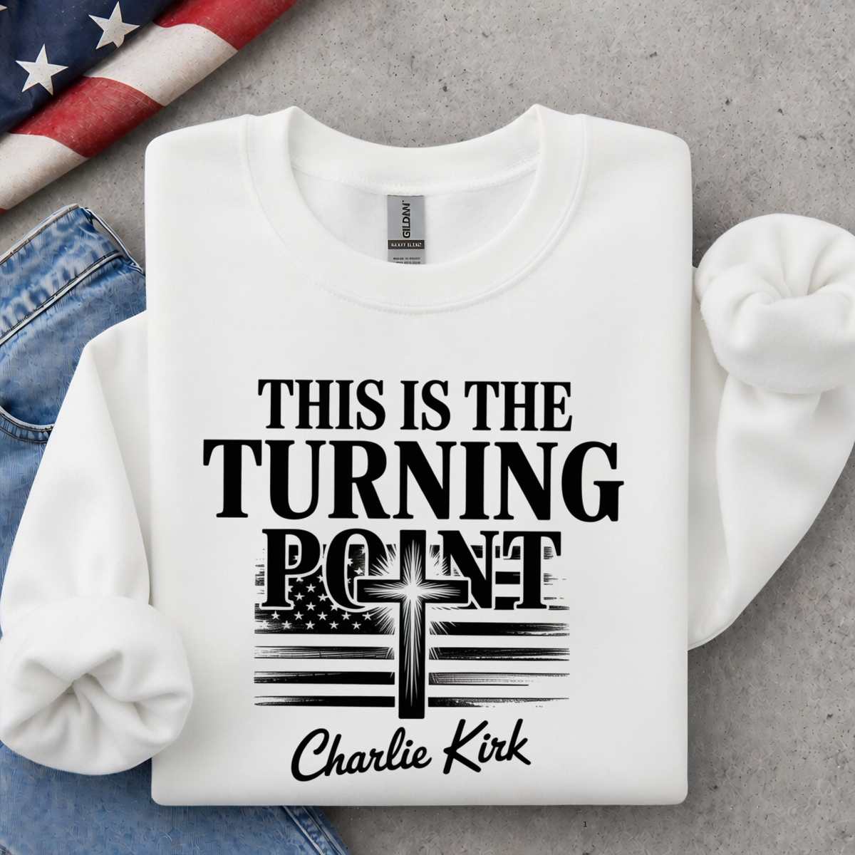 White crewneck sweatshirt flat lay with black This Is the Turning Point lettering, cross, American flag, and Charlie Kirk signature graphic.