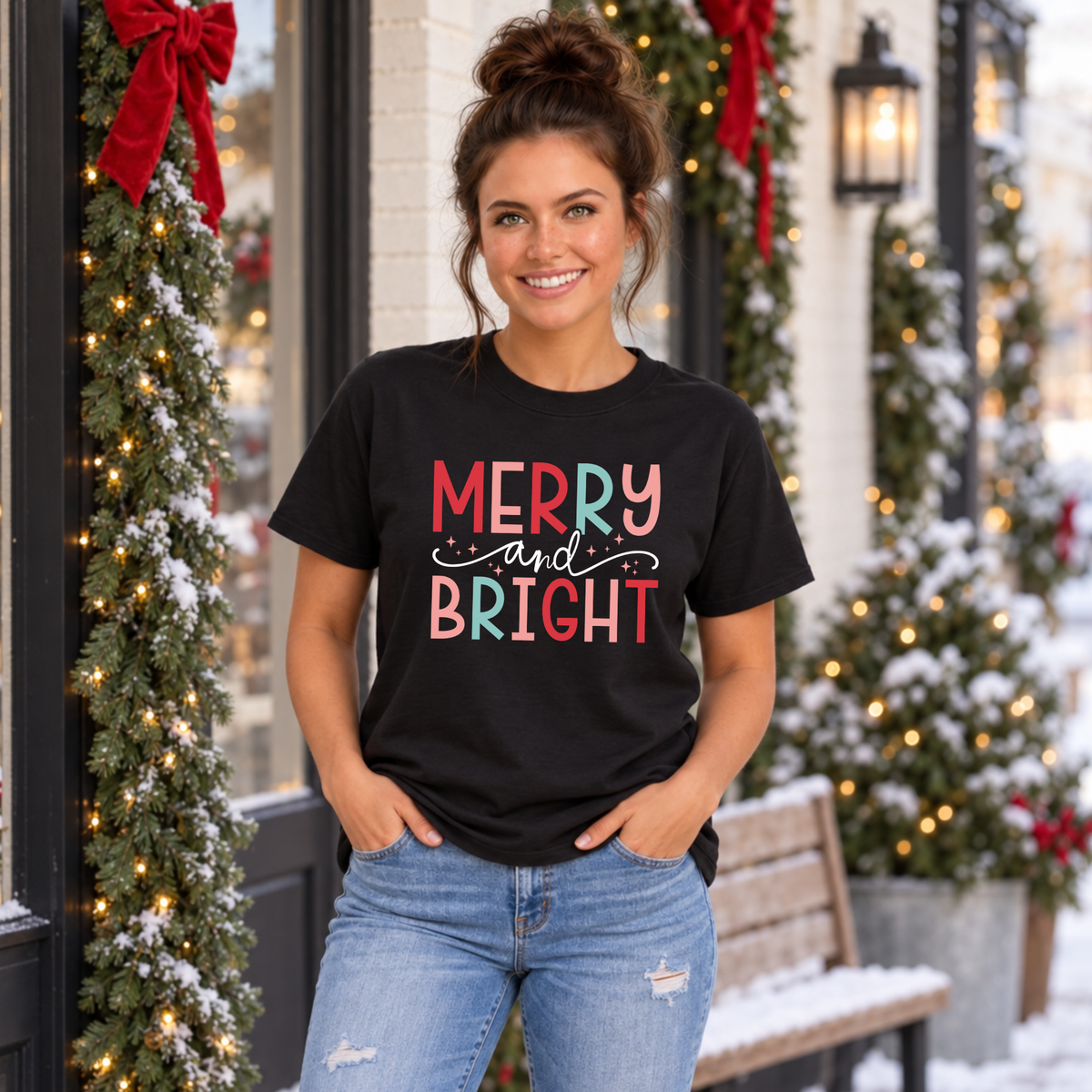 Woman wearing a black T-shirt with colorful Merry and Bright Christmas design outside a snowy holiday storefront