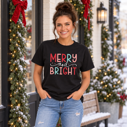 Woman wearing a black T-shirt with colorful Merry and Bright Christmas design outside a snowy holiday storefront