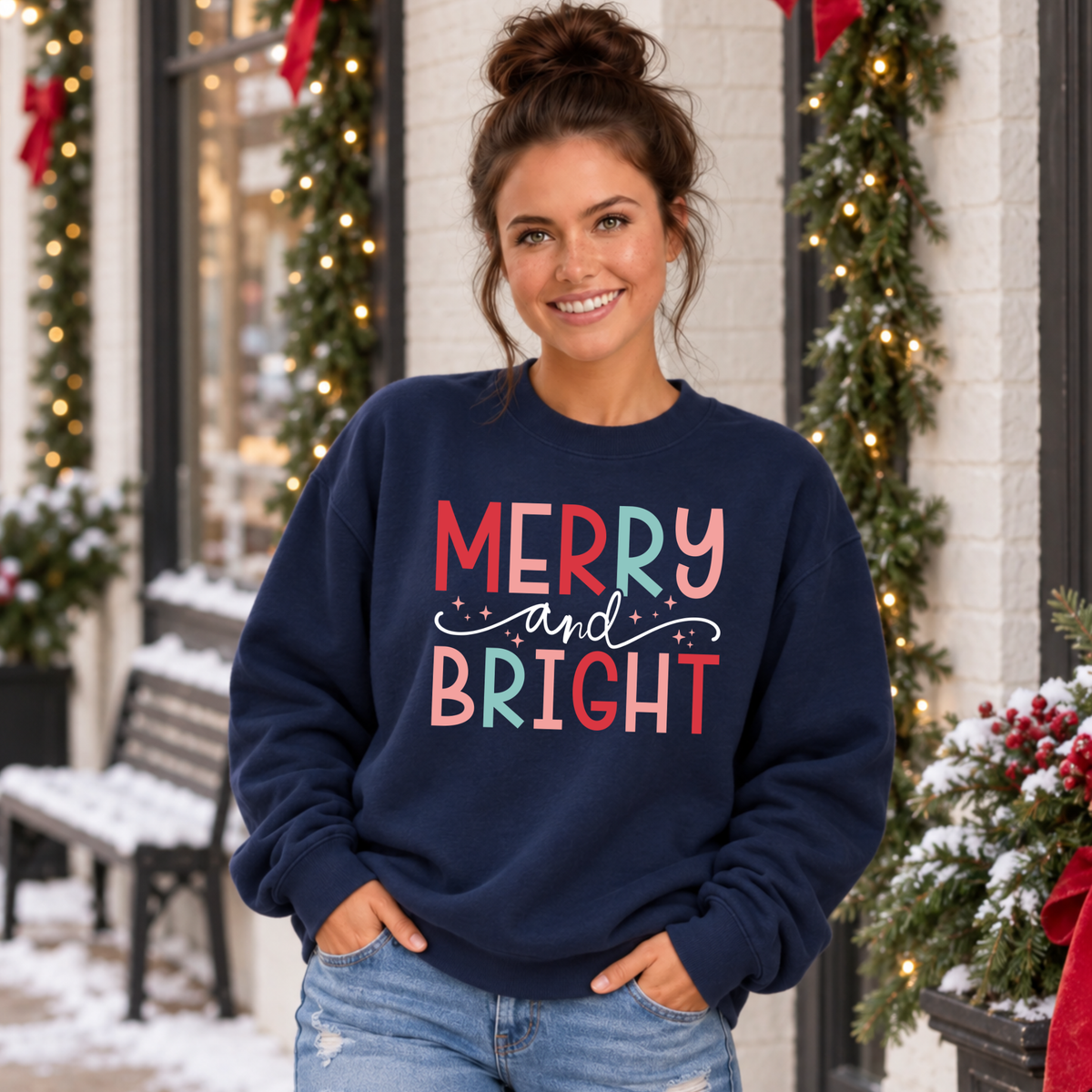 Woman wearing a navy sweatshirt with colorful Merry and Bright Christmas design outside a snowy decorated storefront
