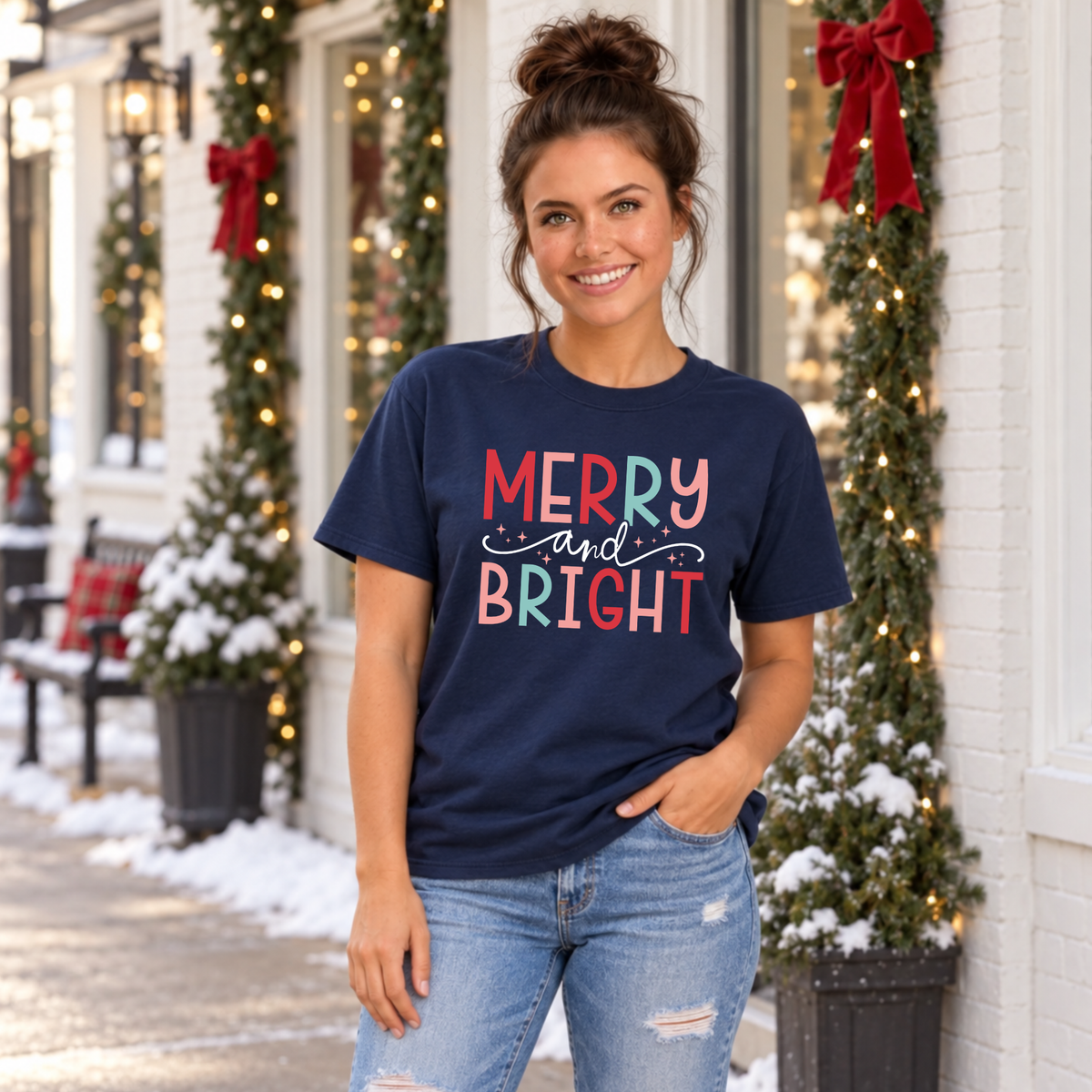Woman wearing a navy T-shirt with colorful Merry and Bright Christmas design outside a snowy holiday storefront