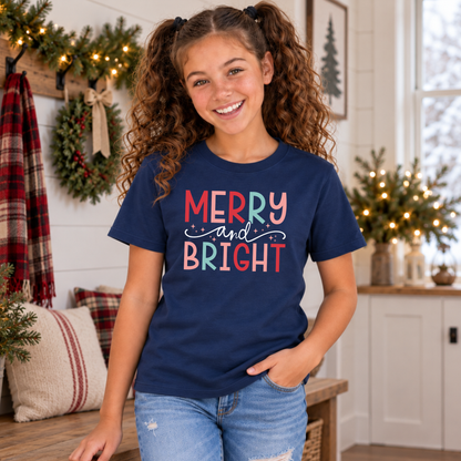 Girl wearing a navy youth T-shirt with colorful Merry and Bright Christmas design in a cozy holiday home