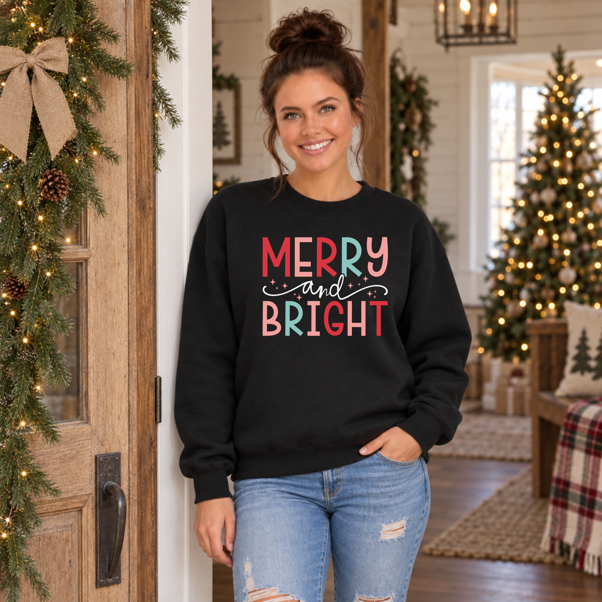 Woman wearing a black sweatshirt with colorful Merry and Bright Christmas design in a decorated doorway