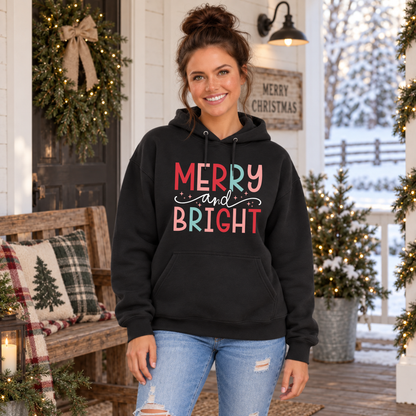 Woman wearing a black hoodie with colorful Merry and Bright Christmas design on a snowy decorated porch