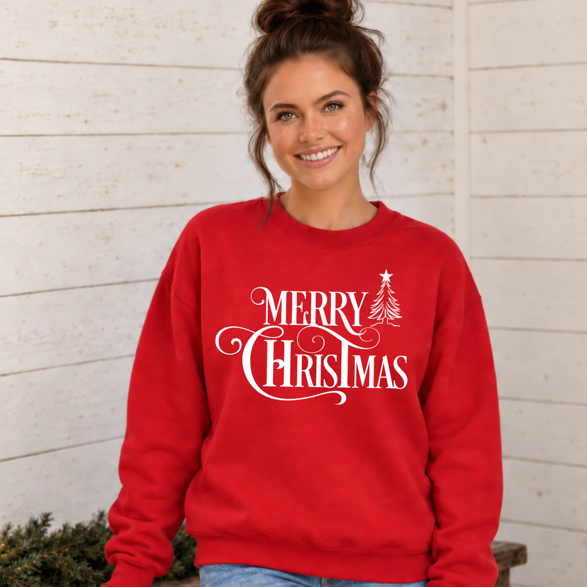 Red crewneck sweatshirt featuring the white Merry Christmas and tree graphic, worn in a rustic holiday room.