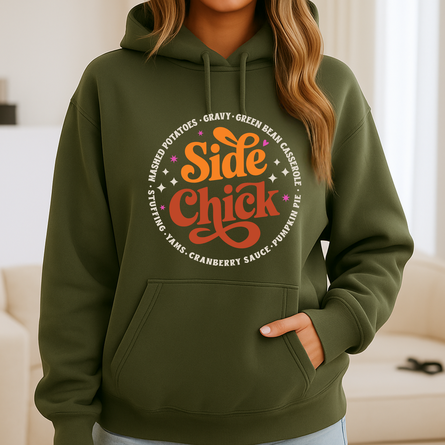 Military green “Side Chick” hoodie shown on woman in casual indoor setting. Thanksgiving-themed design with retro fonts and colorful stars. Great fall fashion hoodie for women or unisex wear.