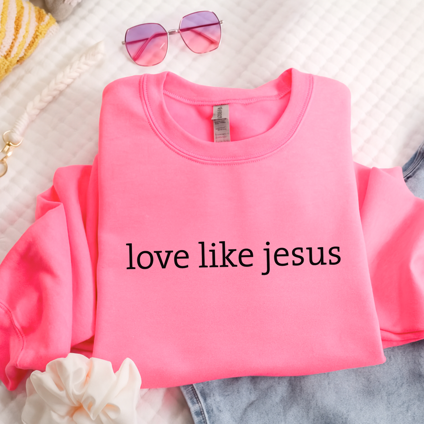 Pink sweatshirt with 'love like jesus' text on a textured surface
